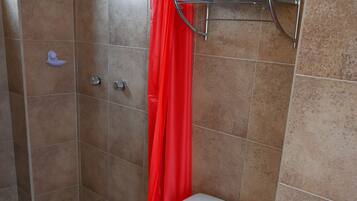 A bathroom with a white toilet, a shower with a red curtain, and a metal shelf.