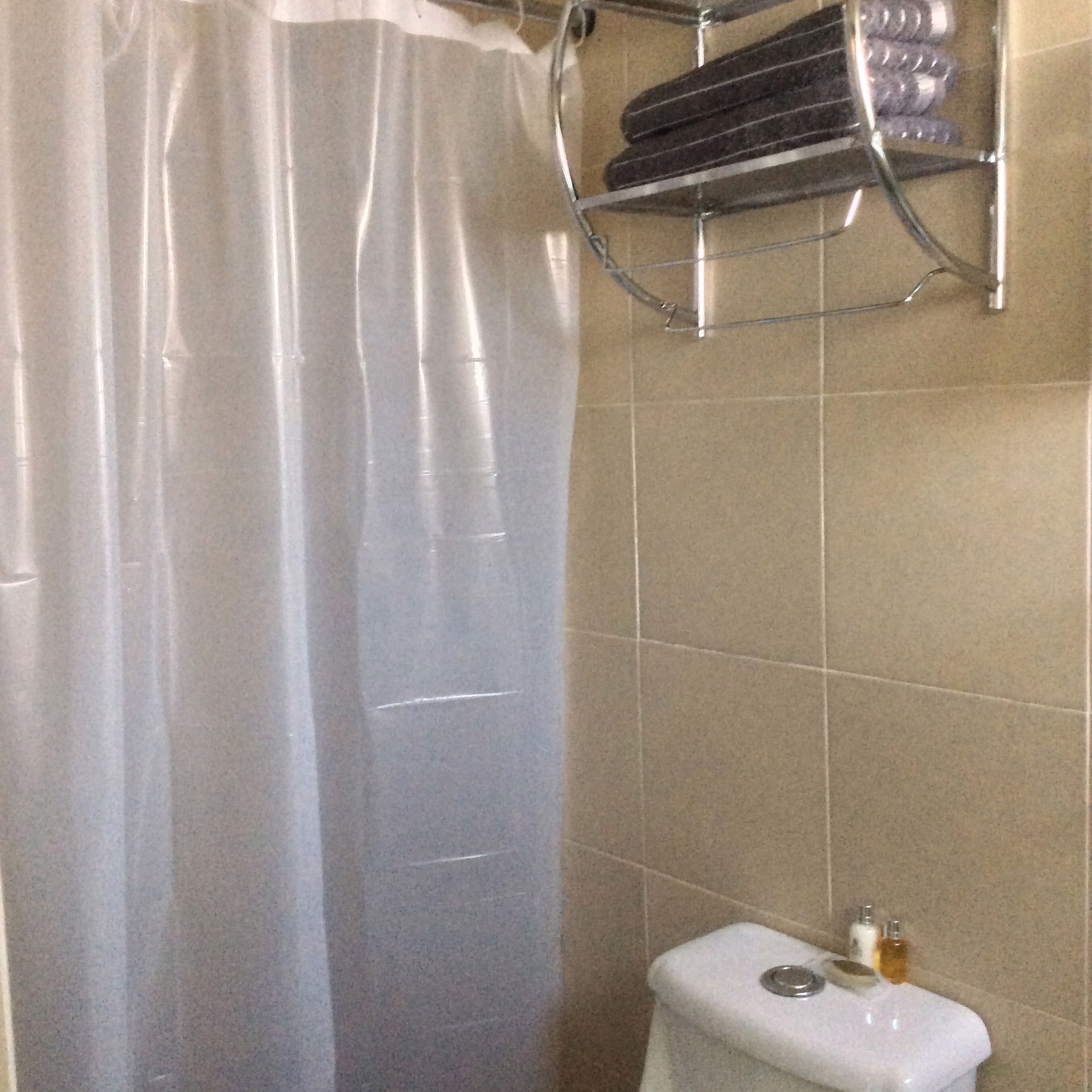 A bathroom with a shower curtain, a toilet, and a shelf with toiletries.