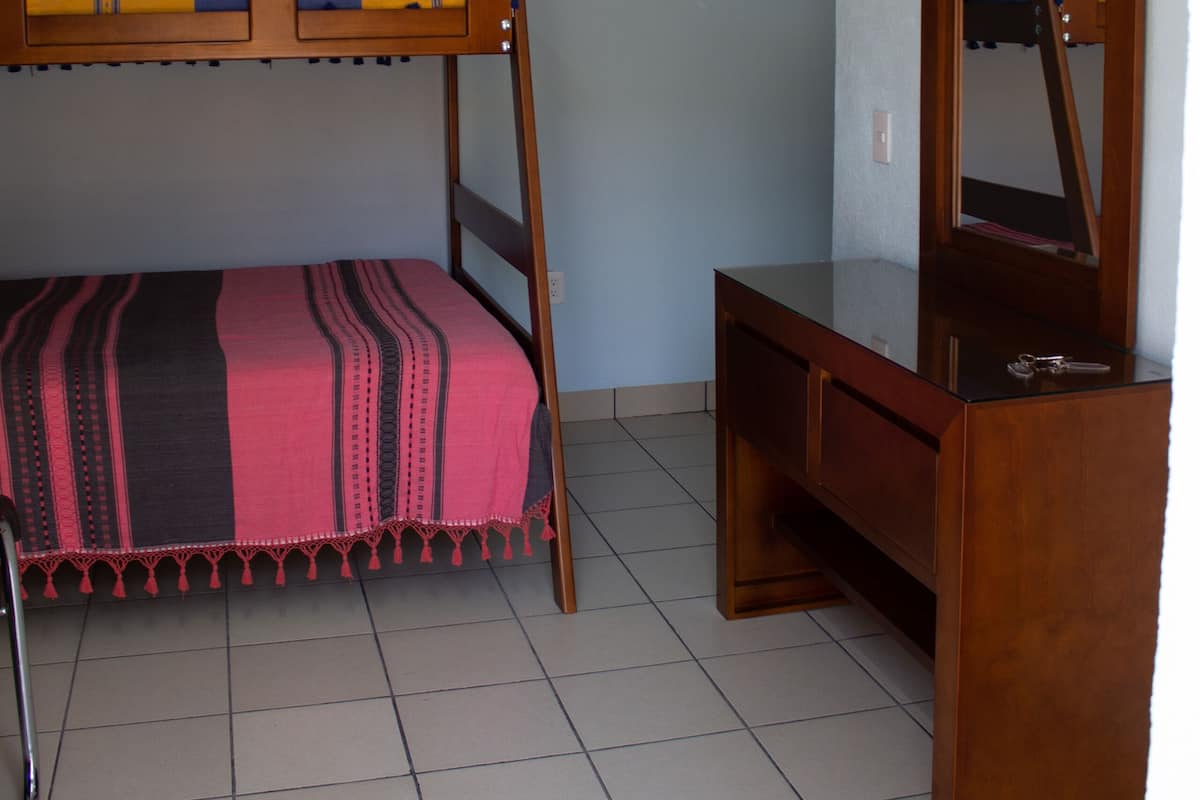 A room with a bunk bed, a wooden desk, and a mirror.