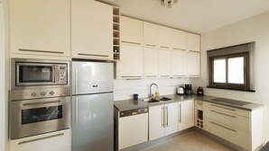 Een moderne keuken met roestvrijstalen apparatuur, witte kastjes en een raam met jaloezieën.