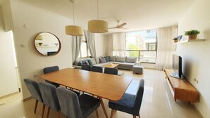 Een moderne woonkamer met een eethoek, een zithoek, een televisie en een plafondventilator.