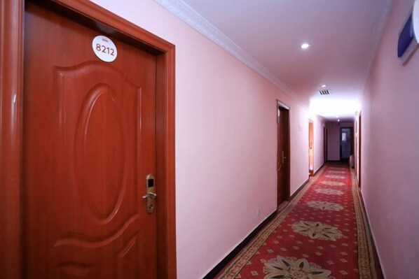 A hallway with a red carpet, wooden doors, and a number sign on one door.