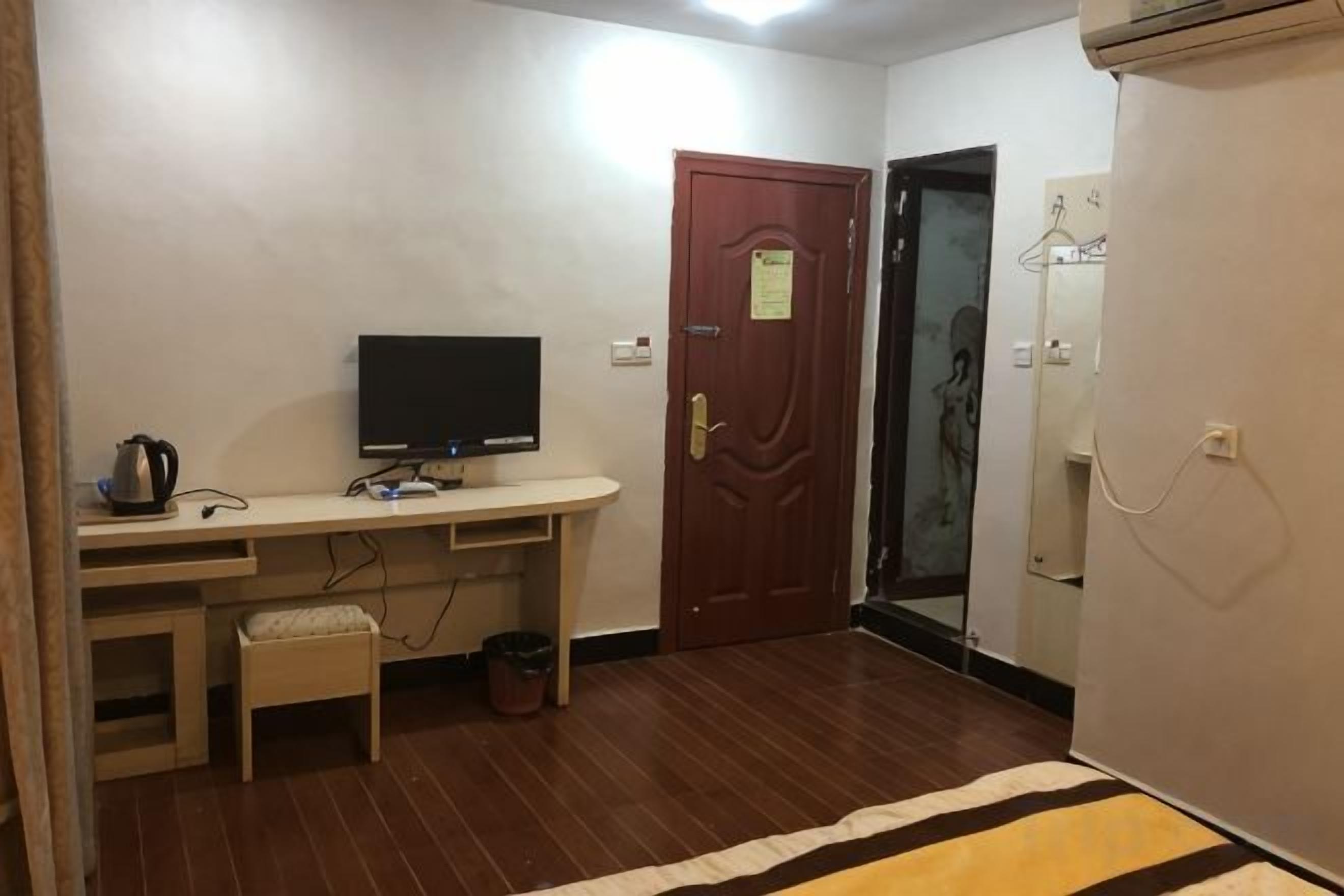 Une pièce avec un bureau en bois, une télévision, une porte avec une pancarte et un miroir.