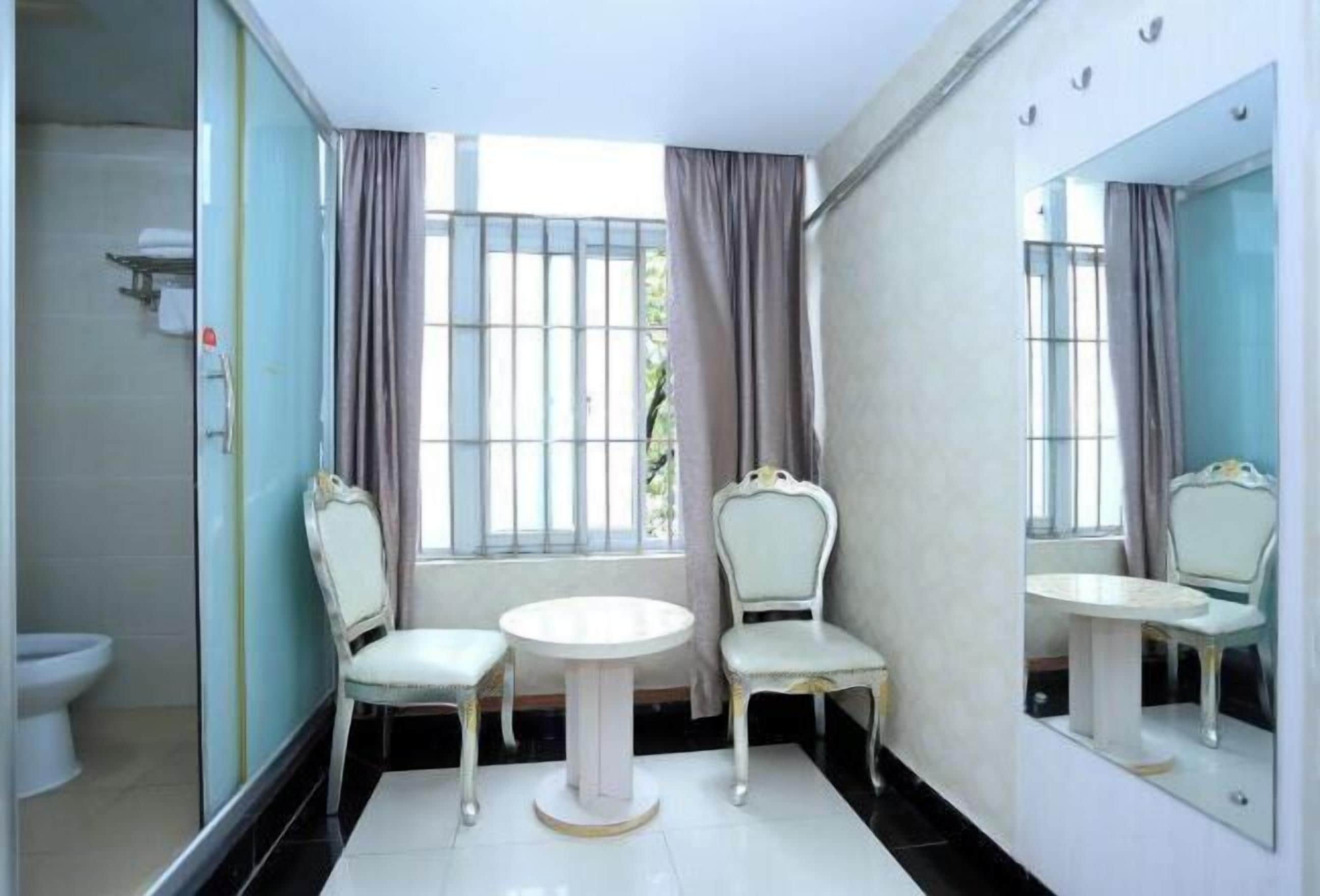 A bathroom with a toilet, two chairs, a round table, and a large mirror.