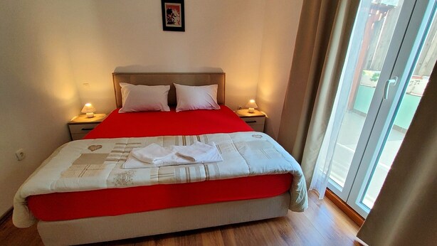 Ein ordentlich bezogenes Bett mit roter Bettdecke und weißen Kissen, zwei Nachttischlampen und ein gerahmtes Bild an der Wand.