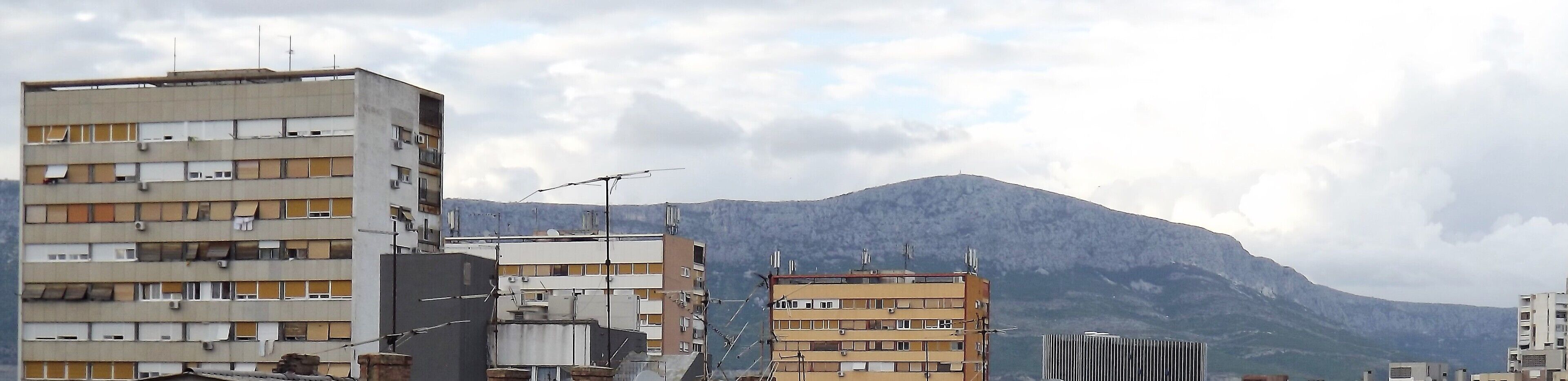 A multi-story building with balconies and air conditioning units, set against a backdrop of a mountain.