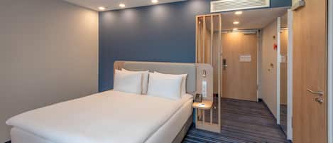Une chambre d’hôtel avec un lit, une table de chevet et une porte donnant sur un couloir.