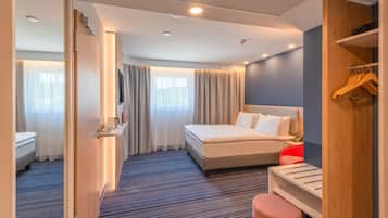 Een hotelkamer met een bed, nachtkastje, spiegel, kledingkast en zithoek.
