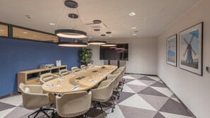 A conference room with a long table, chairs, a projector screen, and a large plant. - Holiday Inn Express Hamburg South A7 As42 (Egestorf)