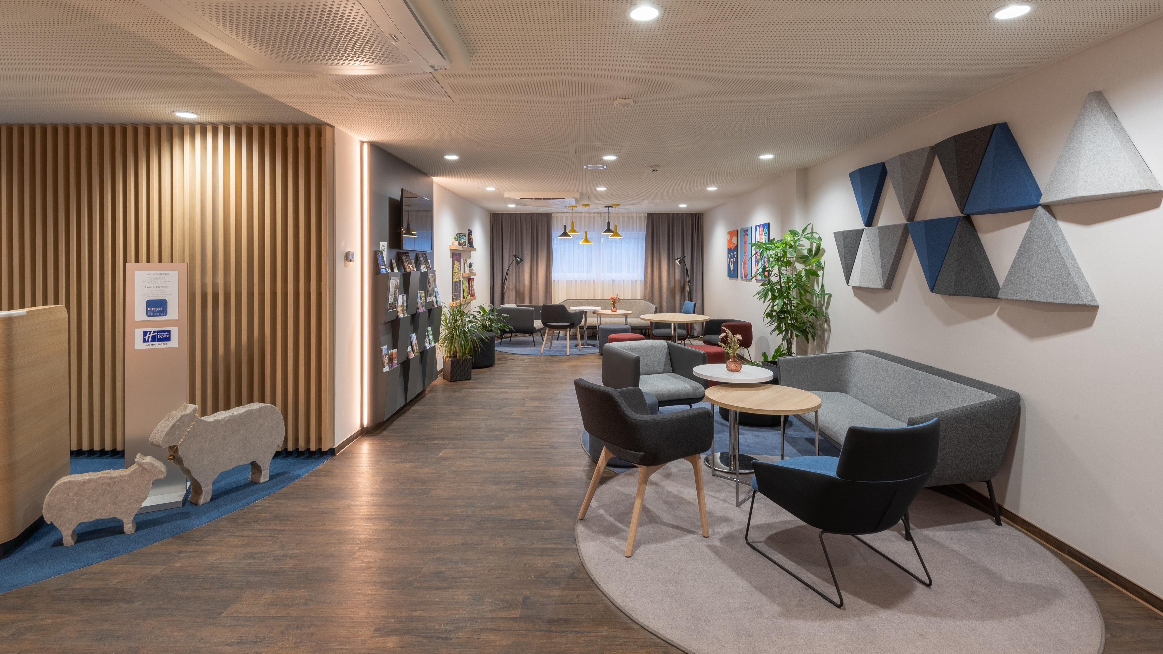 En moderne hotellobby med en træreception, et loungeområde med sofaer og stole, samt en væg med geometrisk vægkunst.