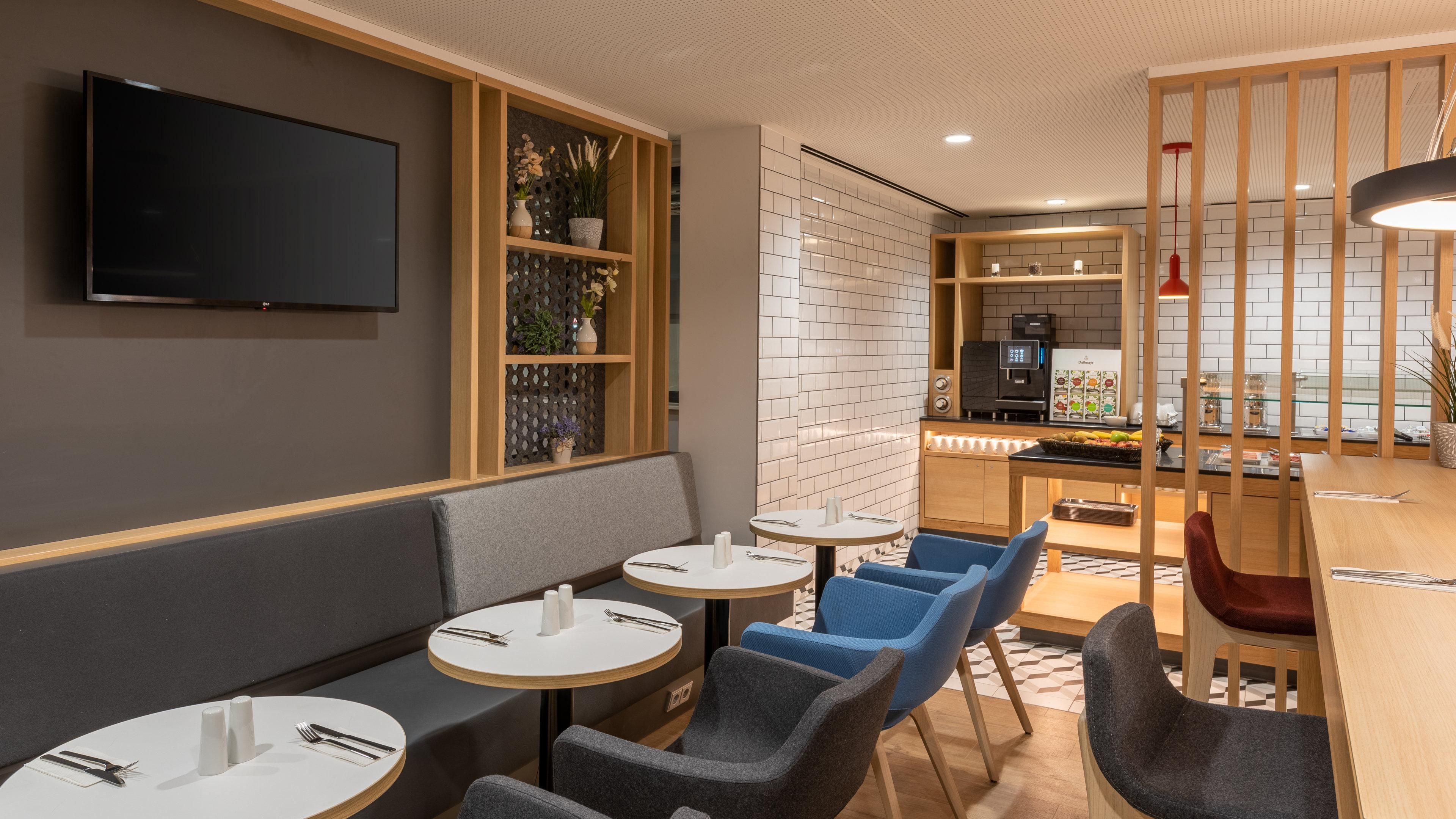 En moderne restaurant med runde borde, blå stole og et barområde.