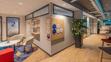 Un espace de bureau moderne comprenant un comptoir d’accueil, un espace détente et une signalétique indiquant les différents services, tels que l’espace de «
coworking
» et l’hôtel.