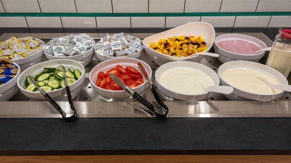 A buffet with various food items including sliced cucumbers, tomatoes, mixed fruits, and different types of dips. - Holiday Inn Express Hamburg South A7 As42 (Egestorf)