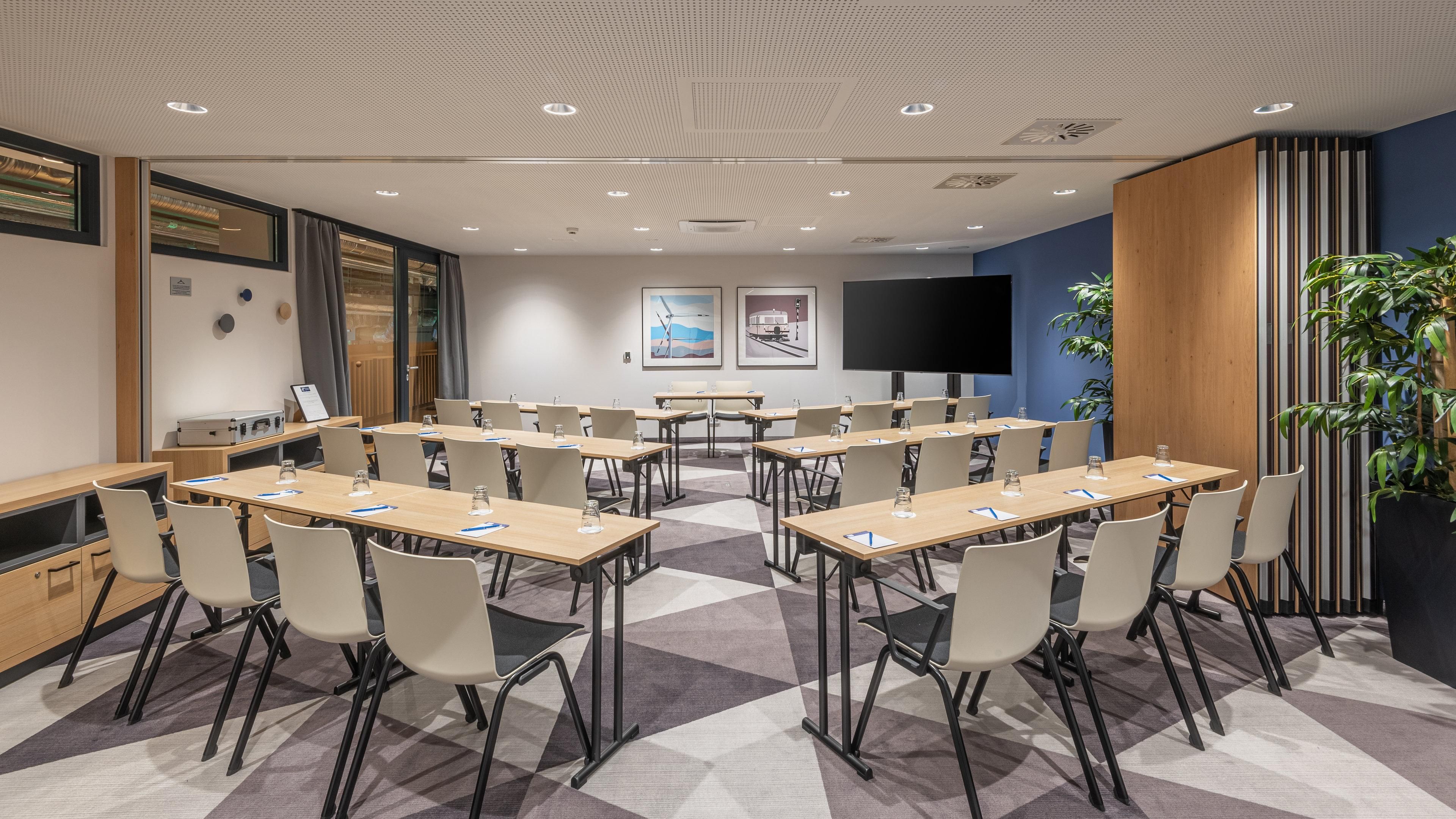 Ett konferensrum med flera bord och stolar, en stor tv-skärm och inramade konstverk på väggarna.