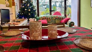Un coin repas avec une nappe à carreaux rouges et verts, trois chandeliers en osier et un sapin de Noël en arrière-plan.