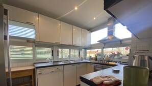 Une cuisine moderne avec des meubles blancs, un lave-vaisselle, une cuisinière et une grande fenêtre équipée de stores.