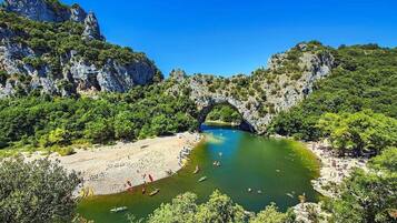 Une arche naturelle enjambant une rivière, avec une plage de sable et de la végétation de chaque côté.