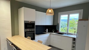 A modern kitchen with white cabinets, a wooden table, and a hanging pendant light. - VILLA 14 Pers. Private pool, pétanque, terrace. 1km from Vallon center (Vallon-Pont-d'Arc)