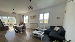 A modern living room with a black sofa, a white coffee table, and a dining area with a table and chairs. - VILLA 14 Pers. Private pool, pétanque, terrace. 1km from Vallon center (Vallon-Pont-d'Arc)