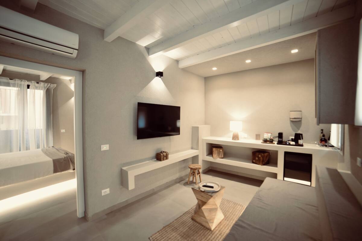 A modern living room with a flat-screen TV mounted on the wall, a sofa, a coffee table, and built-in shelving with various items.