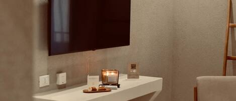 A modern living room with a flat-screen TV mounted on a textured wall, a wooden chair, a small stool, and a white console table with a candle and a QR code sign.
