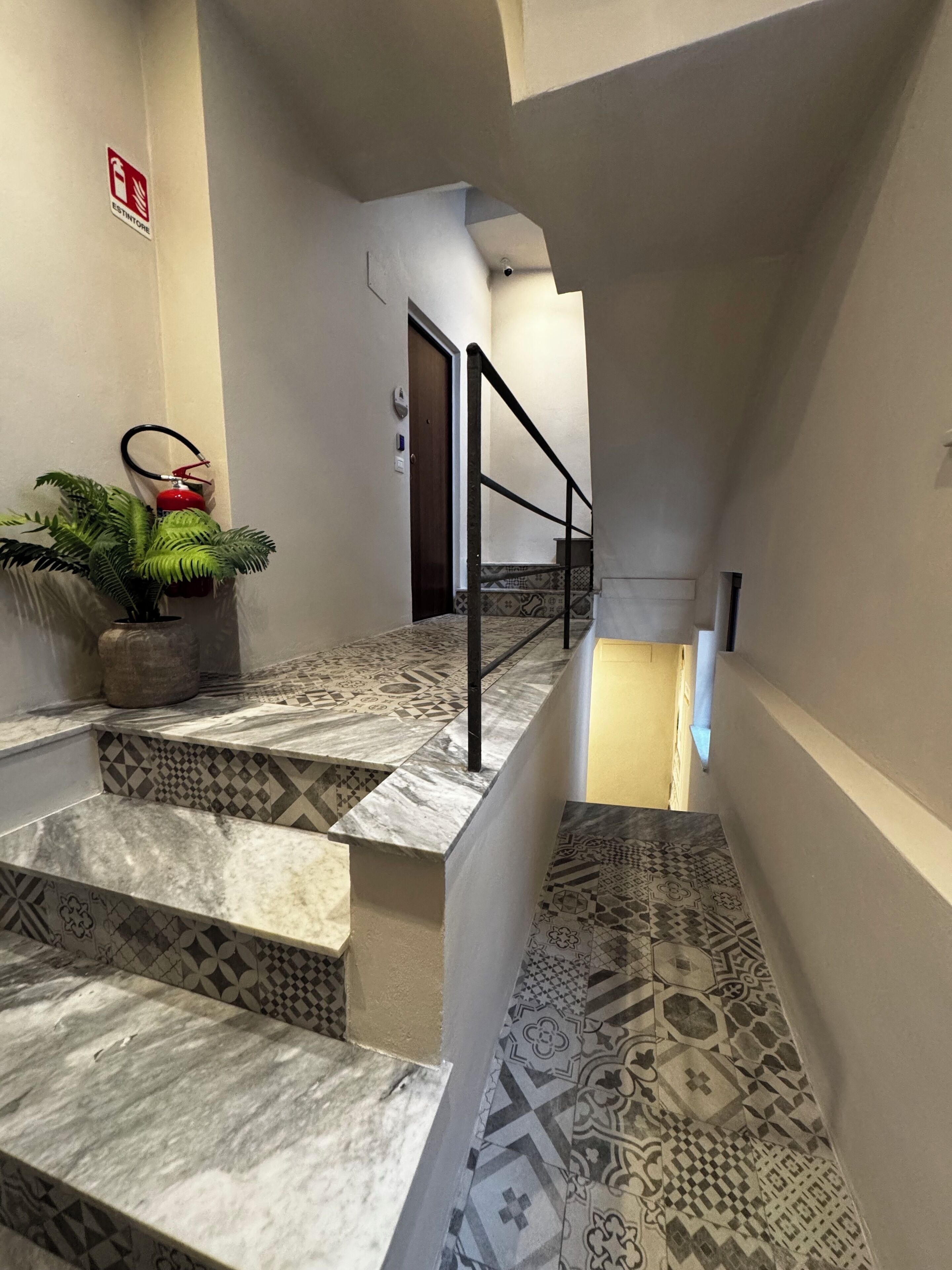Una escalera con baldosas estampadas, una planta en maceta y un extintor.