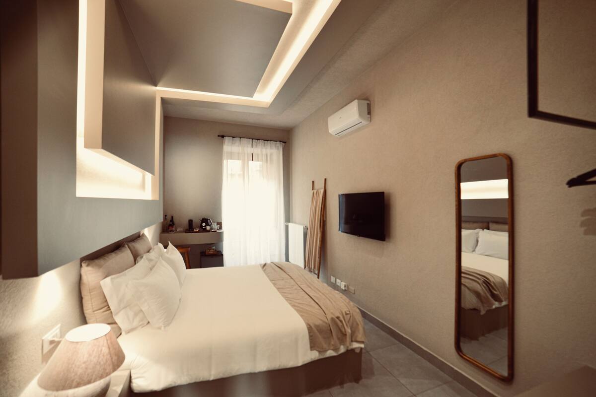 A modern hotel room with a large bed, bedside table, lamp, and a flat-screen TV mounted on the wall.