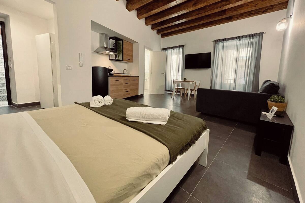 A modern bedroom with a large bed, a desk, a sofa, and a TV.
