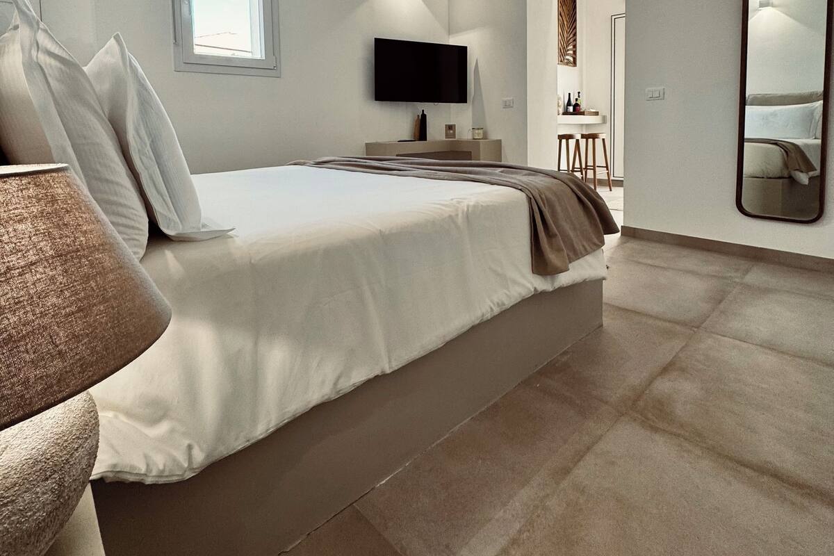 A bedroom with a large bed, a television, a window, and a mirror.