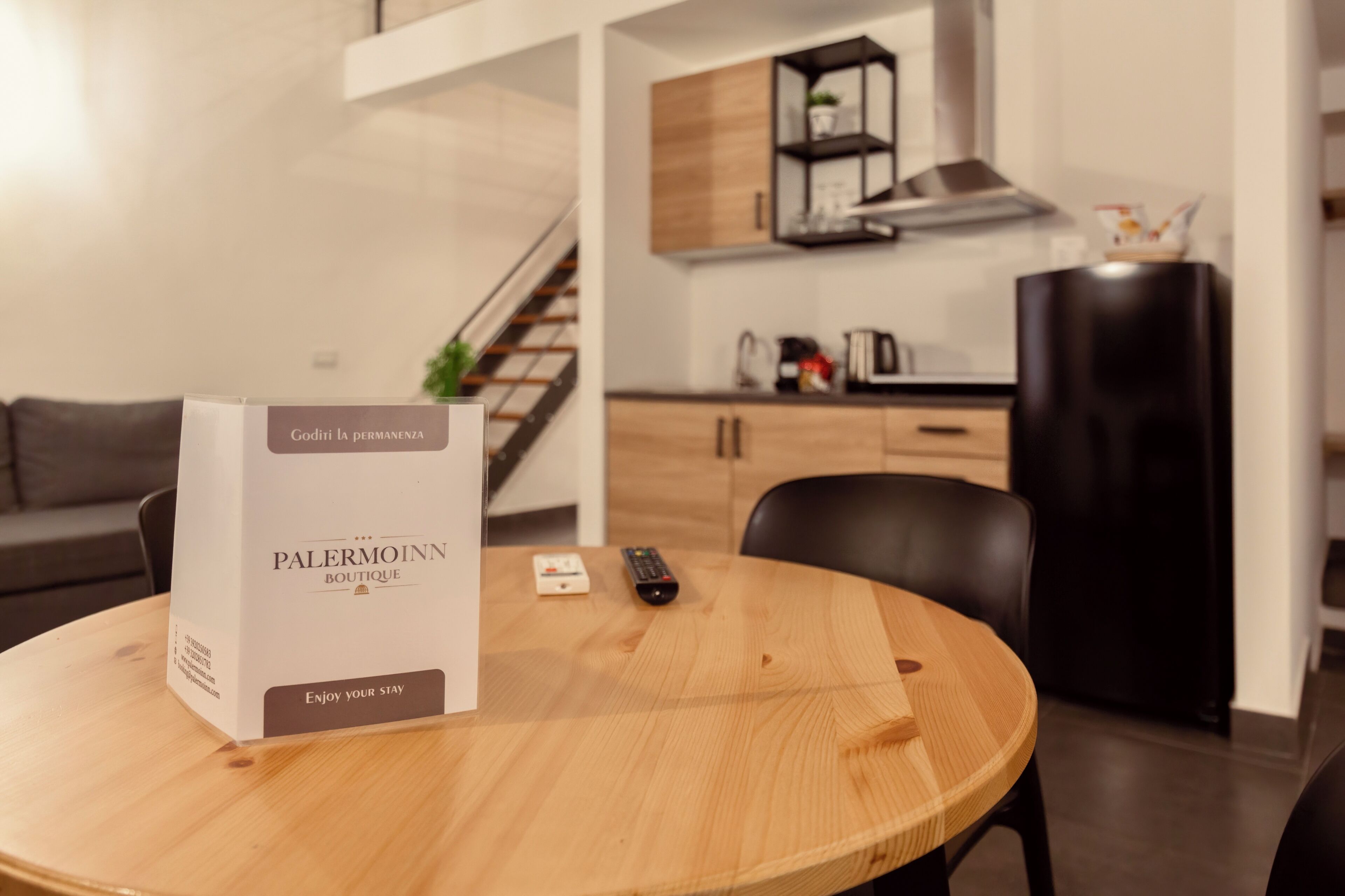 A modern living room with a round wooden table, a remote control, and a box labeled "Palermoinn Boutique."
