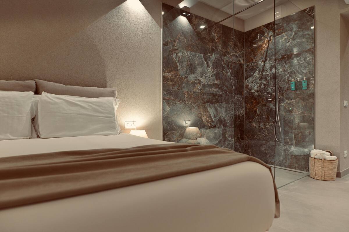 A modern bedroom with a large bed, a glass shower enclosure, and a bedside table with a lamp.