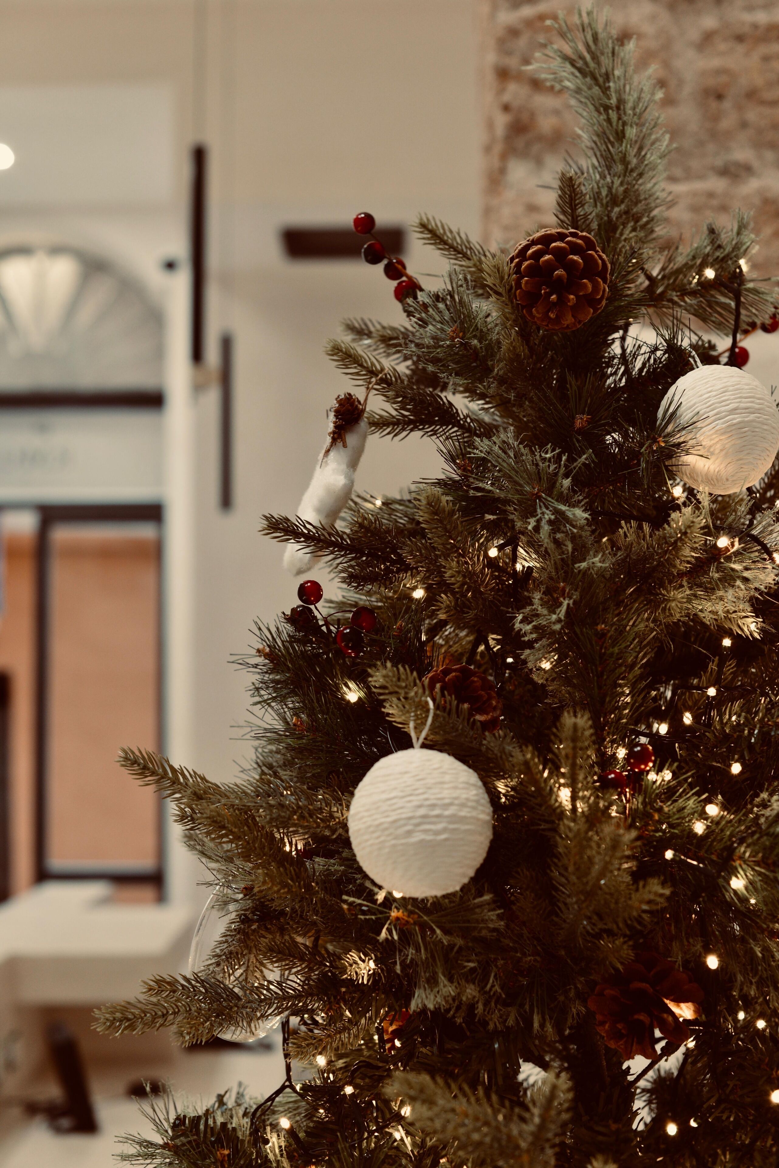A Christmas tree with lights and ornaments, set against a blurred indoor background.