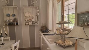 A kitchen with white cabinetry, a dining table with chairs, a small island with a sink, and shelves with kitchenware. - Eumaeos Spitakia (Σύβοτα Λευκάδας)
