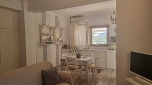 A cozy living room with a sofa and a TV stand, a dining area with a table and chairs, and a kitchen with a window and a sink. - Eumaeos Spitakia (Σύβοτα Λευκάδας)