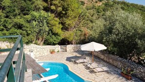 A swimming pool with lounge chairs and a table, surrounded by stone flooring and greenery. - Eumaeos Spitakia (Σύβοτα Λευκάδας)