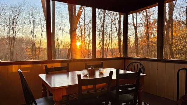 A dining area with a table and chairs, large windows with a view of trees and a sunset. - Lakes and Beaches with Resort Amenities at The Hideout (Hamlin)
