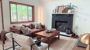 A spacious living room with a high ceiling, a fireplace, and a large window overlooking a forest. - Lakes and Beaches with Resort Amenities at The Hideout (Hamlin)