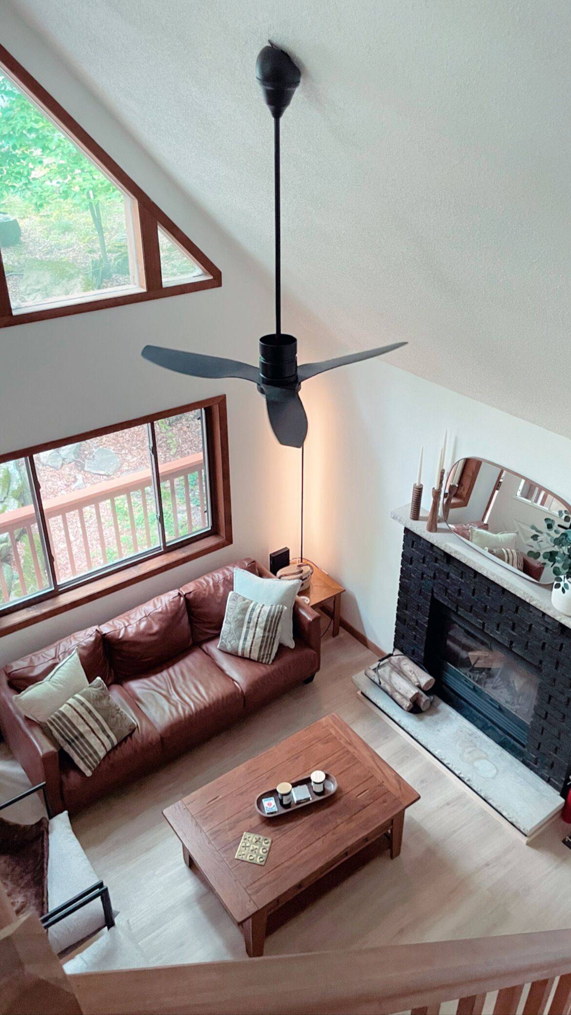 A living room with a brown leather sofa, a wooden coffee table, a fireplace, and a ceiling fan.