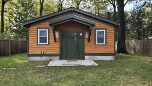 A small wooden cabin with a green door, two windows, and a front porch.
