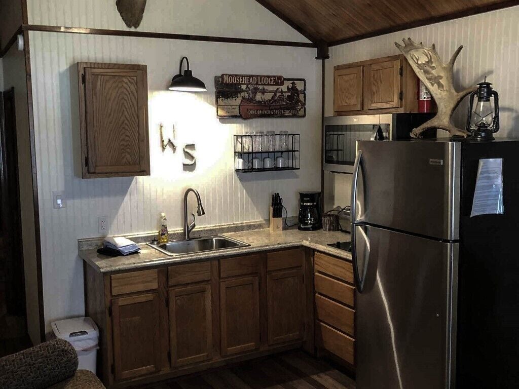 A compact kitchen with wooden cabinets, a stainless steel refrigerator, a sink, and a coffee maker.