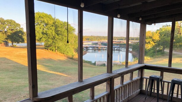 A wooden deck with a view of a lake and boats, a grassy area, and trees. - Willow Springs Marina (Mead)