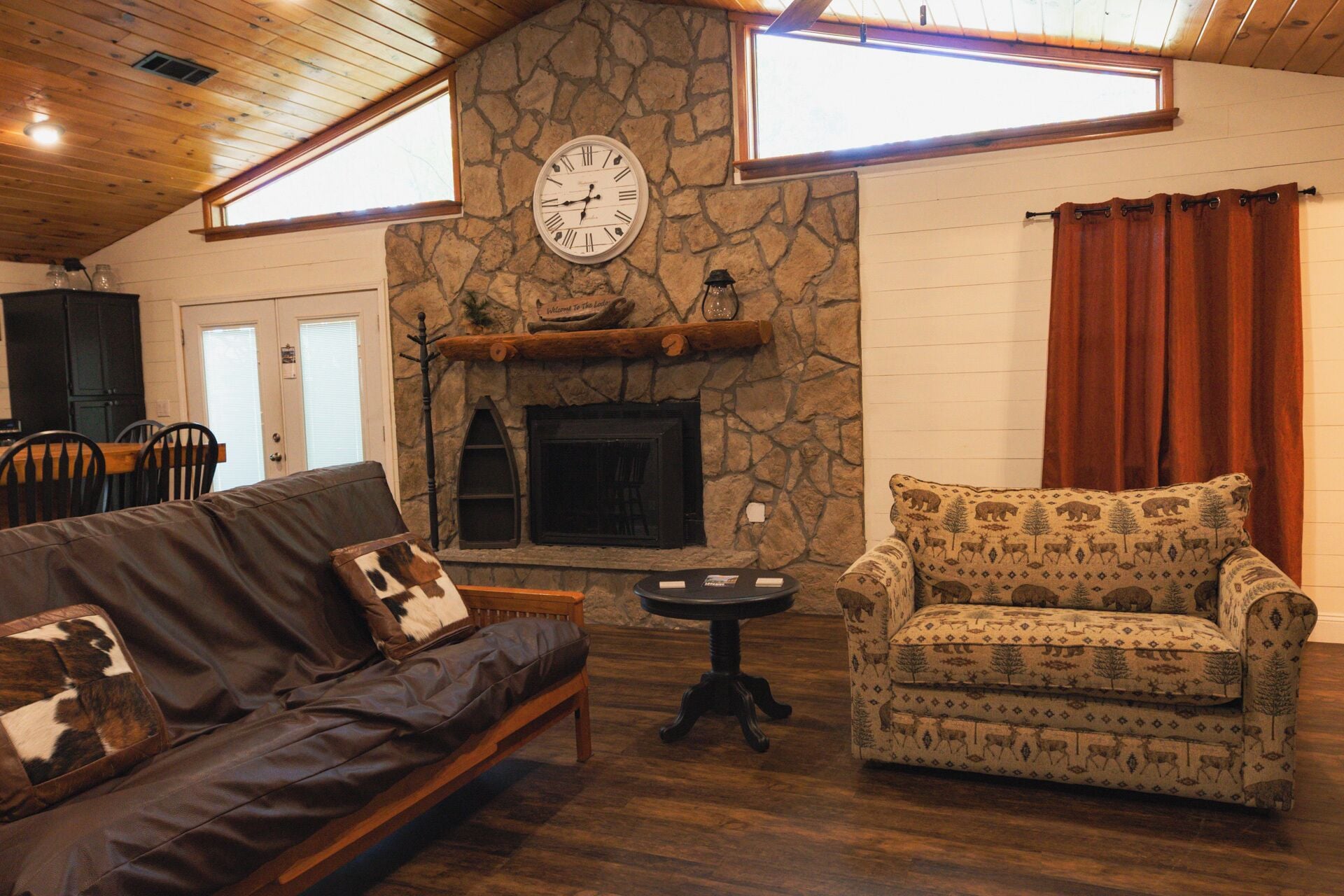 A cozy living room with a stone fireplace, a clock, and a patterned armchair.