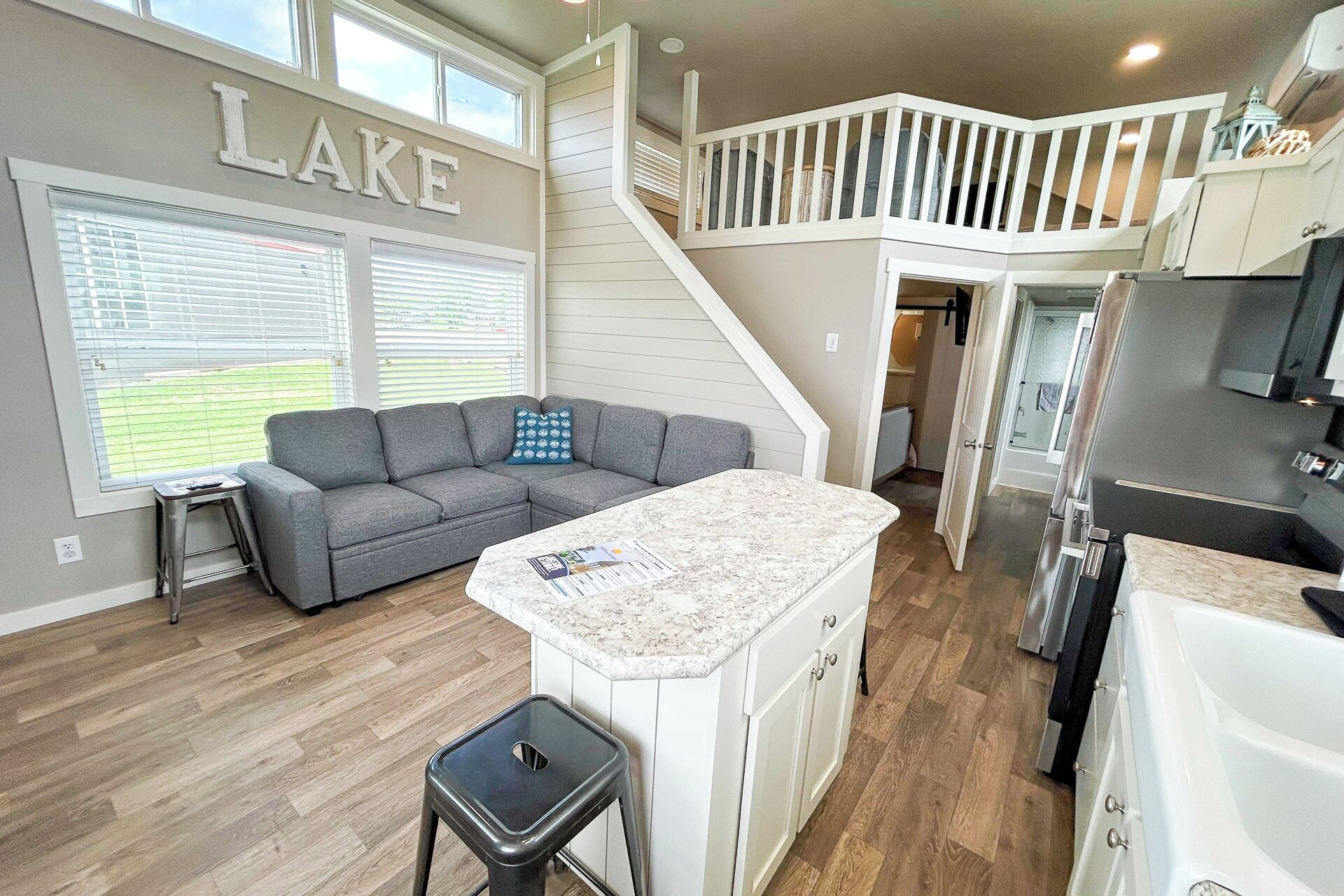 A modern kitchen with a central island, a grey sofa, and a staircase leading to an upper level.