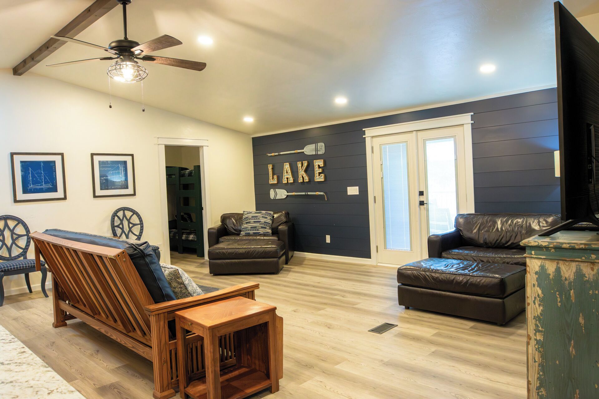 A living room with a wooden bench, two leather sofas, a ceiling fan, and a wall with the word "LAKE" and paddleboard images.