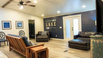 A living room with a wooden bench, two leather sofas, a ceiling fan, and a wall with the word "LAKE" and paddleboard images.