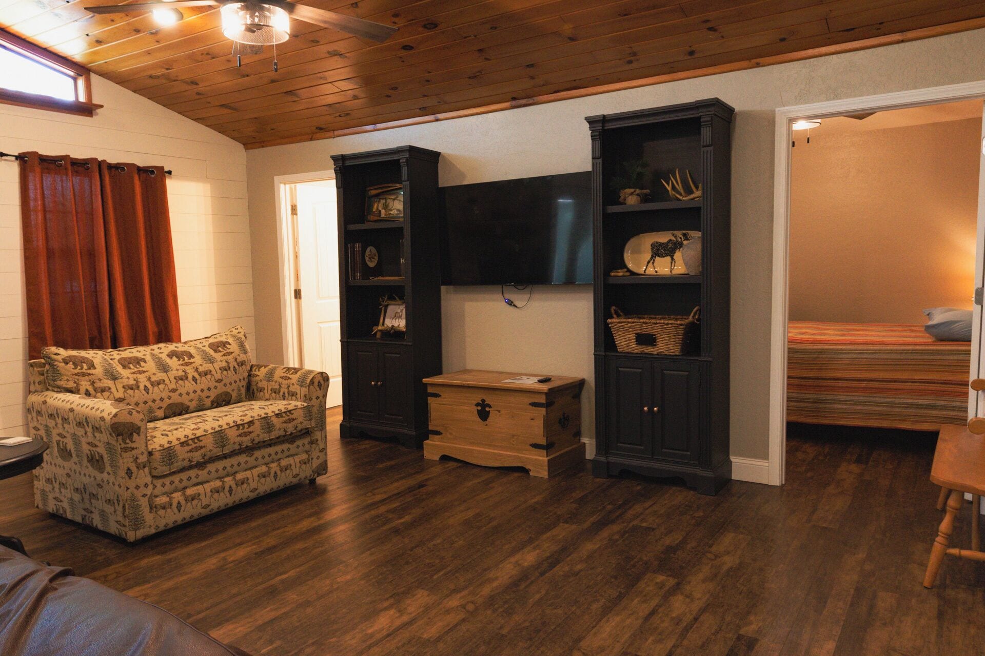 A cozy living room with a patterned sofa, wooden cabinets, a television, and a bed.
