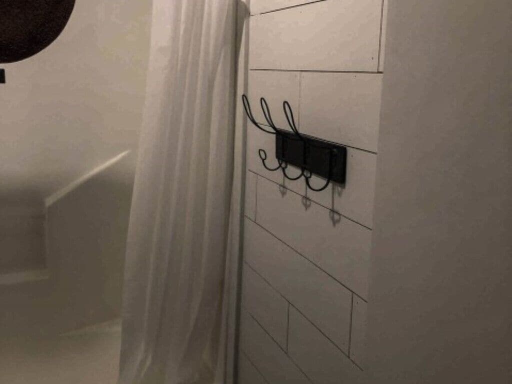 A bathroom with a white tiled wall, a black electrical outlet, and a white shower curtain.