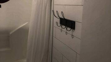 A bathroom with a white tiled wall, a black electrical outlet, and a white shower curtain.