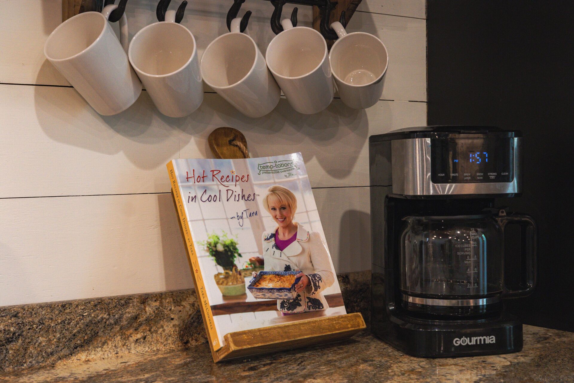 A kitchen counter with a coffee maker and a cookbook titled "Hot Recipes in Cool Dishes" by Tara McConnel.