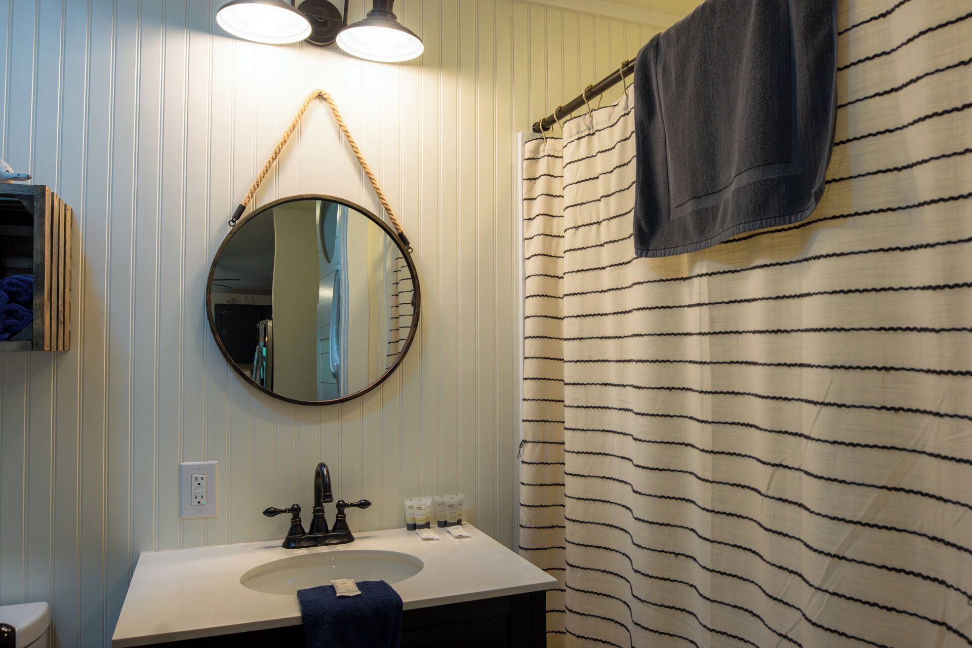 A bathroom with a round mirror, a sink, and a striped shower curtain.